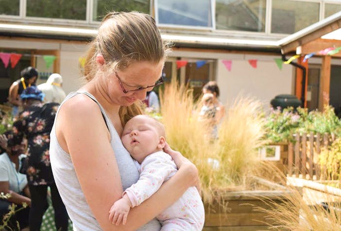 A mum holding her baby at a Lambeth Early Action Partnership garden event.